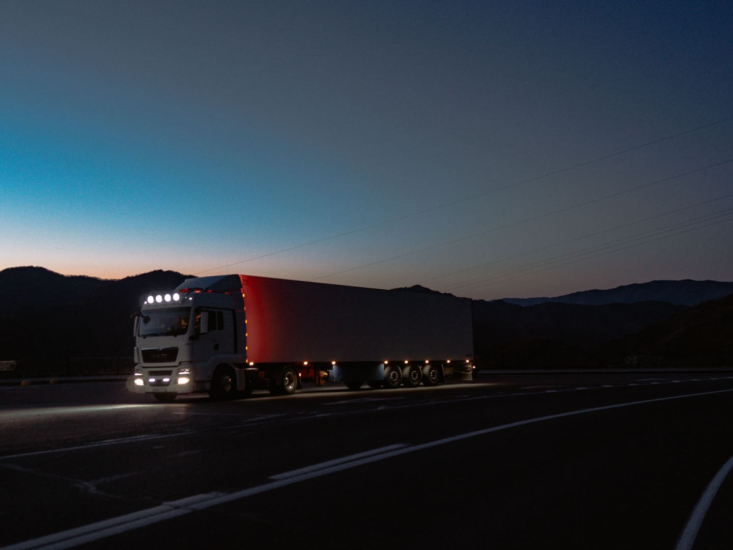 A truck on a mountain road at dusk, its lights on