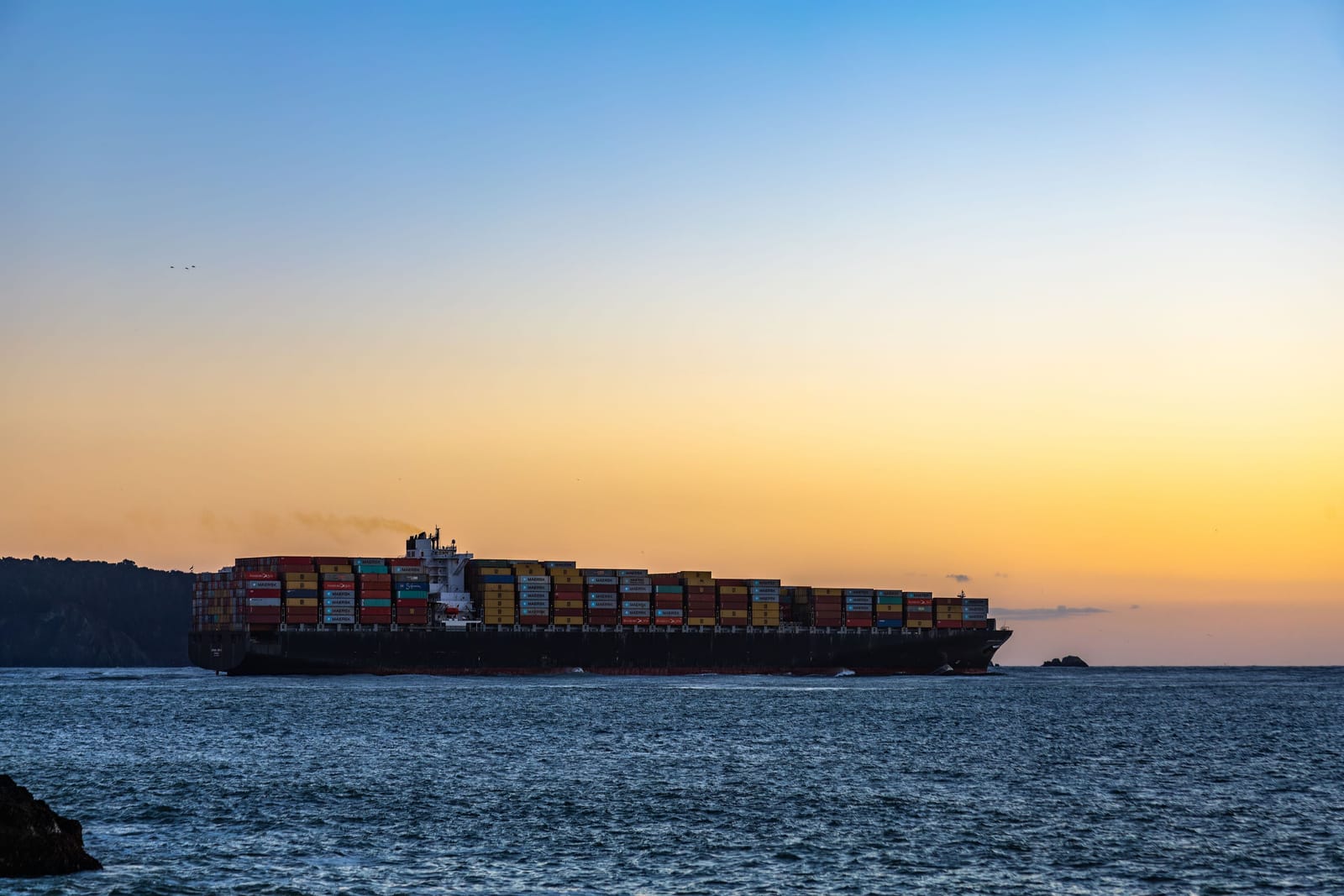 A container ship under way at dusk, an amber sky over a navy sea